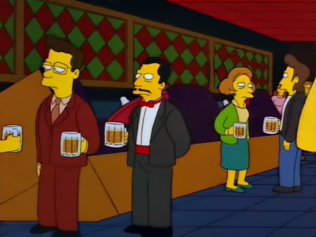 Mr. Burns stands with other party guests in a dim bar, while a man in a maroon sweater and red glasses stands at a counter…