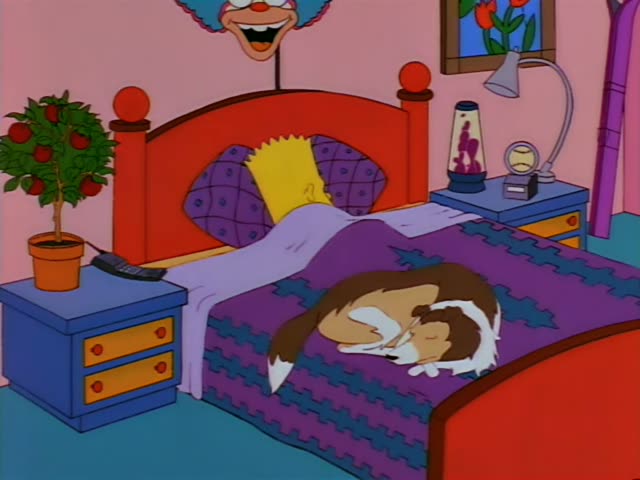 Bart Simpson lies in bed against a purple quilted pillow under a red headboard, holding a large black cordless phone…