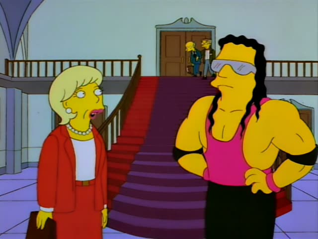 A blonde woman in a red suit with a pearl necklace and a briefcase stands talking with a muscular man in a pink tank top…