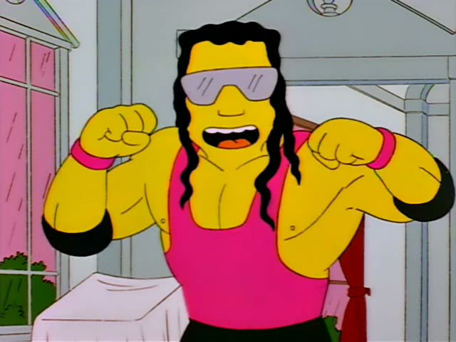 A muscular man with long dark curly hair, visor sunglasses and a pink tank top flexes his arms in a pale room with a white…