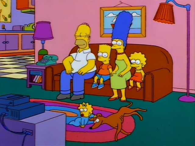 Homer, Marge, Bart, Lisa and Maggie sit on their brown couch in the living room, with Santa's Little Helper the greyhound…