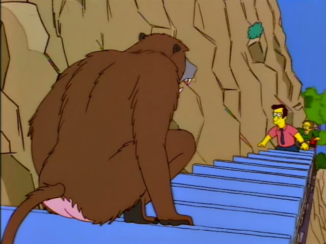 Ned Flanders drives a small red locomotive along a cliff-side track while a man in a pink shirt and tie rides in the blue…