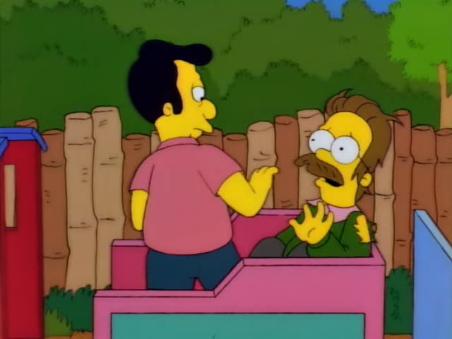 Ned Flanders sits behind a pink car-like structure while a black-haired man in a pink shirt and blue tie stands at its side