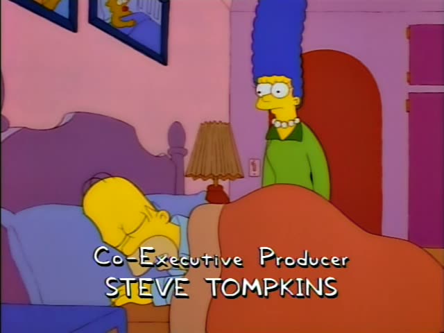 Homer lies asleep under an orange blanket in a bed with a purple headboard, a lamp on the nightstand beside him, while Marge…