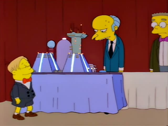 Mr. Burns stands behind a draped table beside Smithers, who wears glasses and a pink bow tie, in front of a red curtain