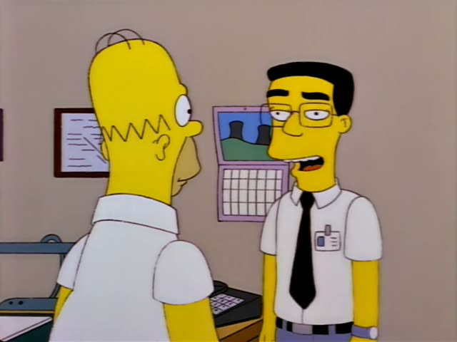 Homer Simpson stands in a beige office with a framed certificate and a calendar on the wall, talking with a thin…