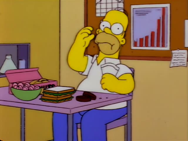Homer Simpson sits at a lilac table in a break room, first lifting a hand to his face and then holding a sandwich and eating…