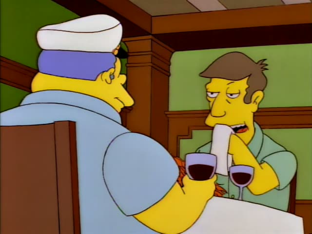A heavy man with blue hair in a white captain's cap and blue shirt sits at a restaurant table with a glass of red wine…