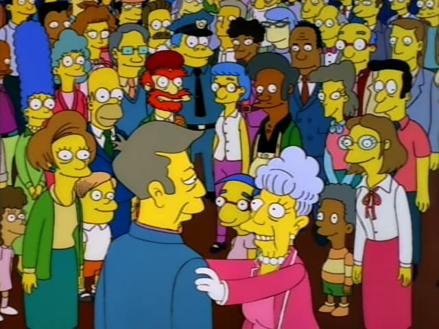 Principal Skinner stands in a crowd of applauding townspeople while an elderly woman in a pink coat, pearl necklace…