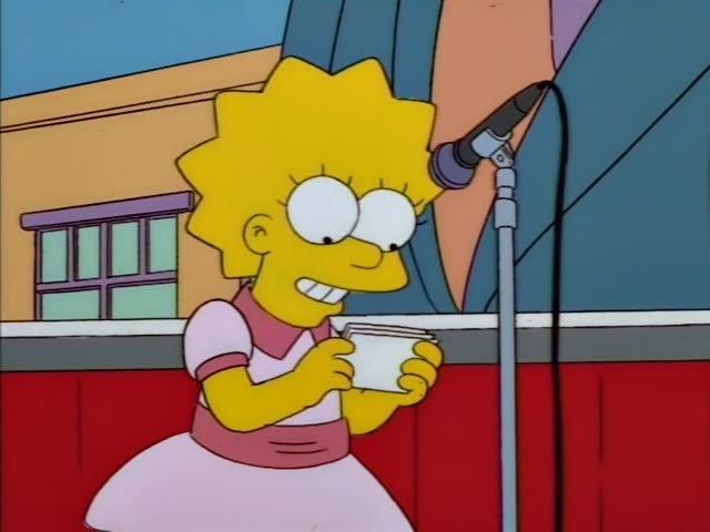 Lisa Simpson stands on a stage beside a microphone on a stand, holding a small stack of cards and smiling, then laughing…