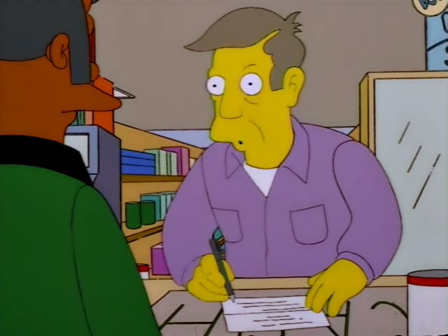 A balding-free man with swept-back brown hair and a lavender shirt stands behind a store counter with a pen and paper…