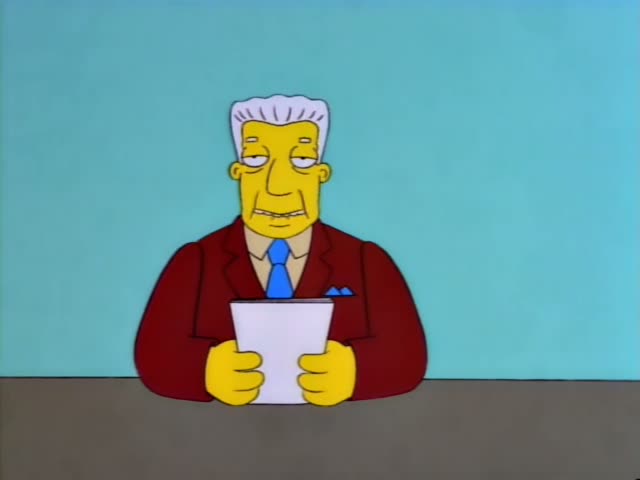 Kent Brockman sits at a desk against a teal wall holding a sheet of paper and reading from it