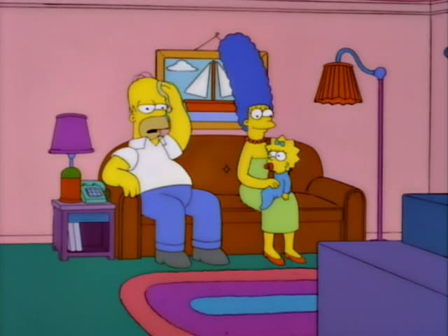 Homer sits on the brown couch in the living room with a phone held to his ear, while Marge with her tall blue beehive stands…