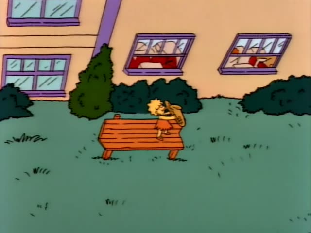 Lisa sits alone on a wooden bench on a grassy lawn in front of a tan school building with purple-trimmed windows…