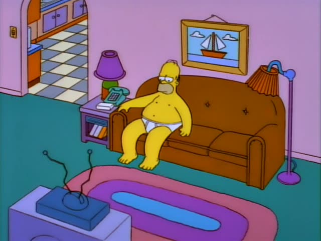 Homer sits slouched on the brown couch in the living room, one arm draped over the armrest and his feet dangling…