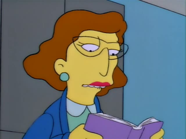 Mrs. Krabappel sits in a classroom reading from a purple book to seated children