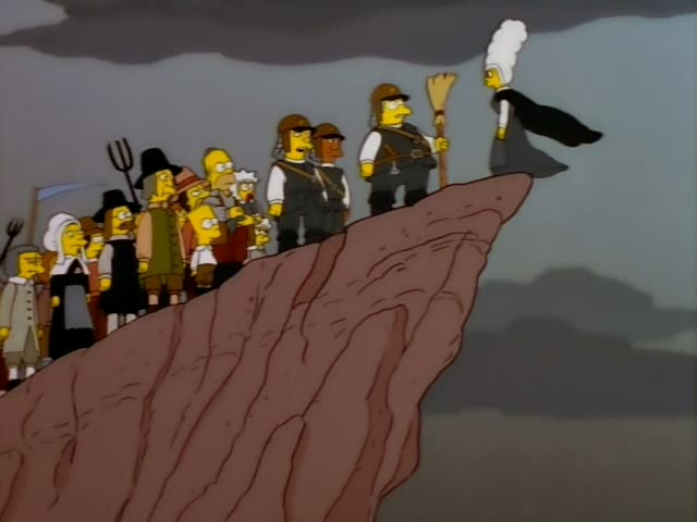 On a rocky cliff edge under a grey sky, a crowd of villagers in Puritan dress, including Homer and Grampa, stands…