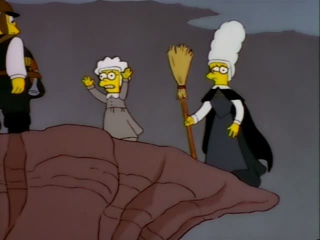 A caped woman in a tall white wig and black cloak holds a broom on a rocky ledge, while a small girl in a grey dress…