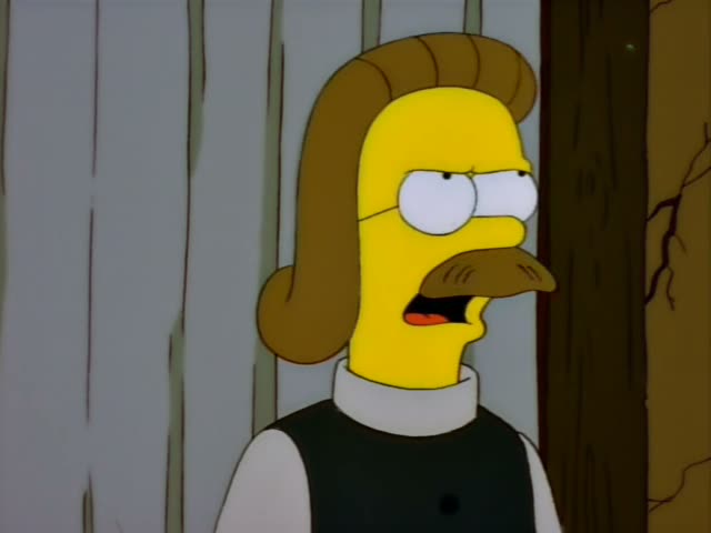 Ned Flanders stands in front of a grey plank wall beside a dark wooden post