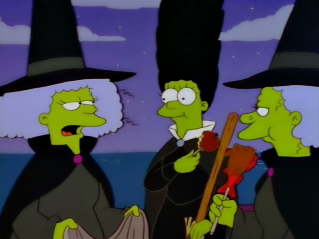 Three green-skinned witches stand against a dusky purple sky over dark water