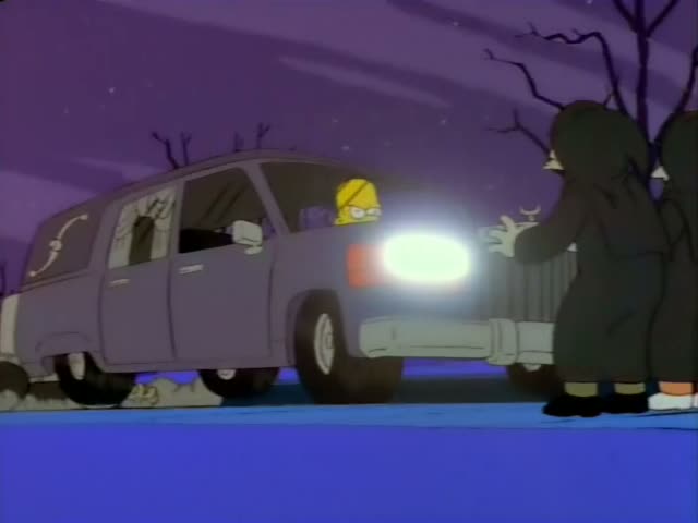 Homer Simpson is driving a grey car while robed, hooded figures climb over it and hang from its sides, one holding a torch…