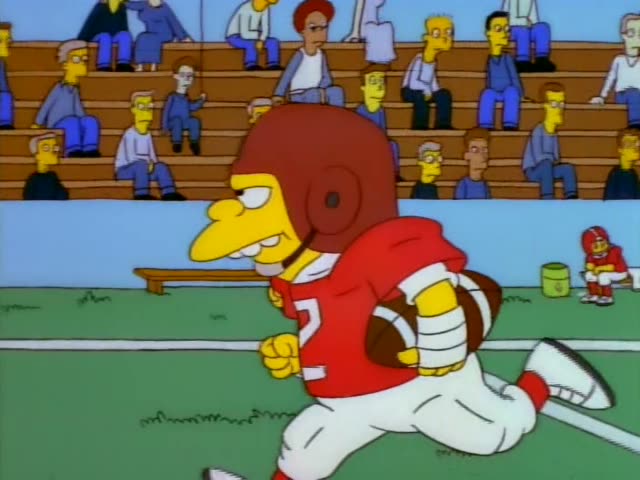 On a football field with a yellow goalpost and bleachers behind, a yellow-skinned player in a red jersey numbered 2…