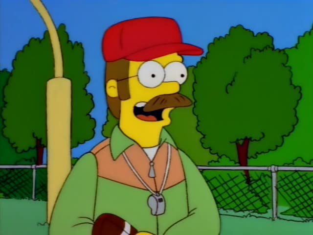 Lisa Simpson and Ned Flanders stand on a grassy field beside a chain-link fence with bushes and trees behind them