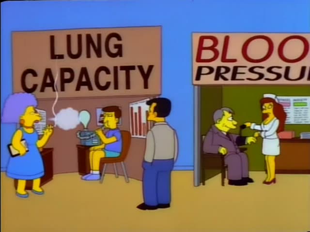 Homer sits in a chair beside a table at the purple-walled Check Your Cholesterol booth, where a man in a white lab coat…