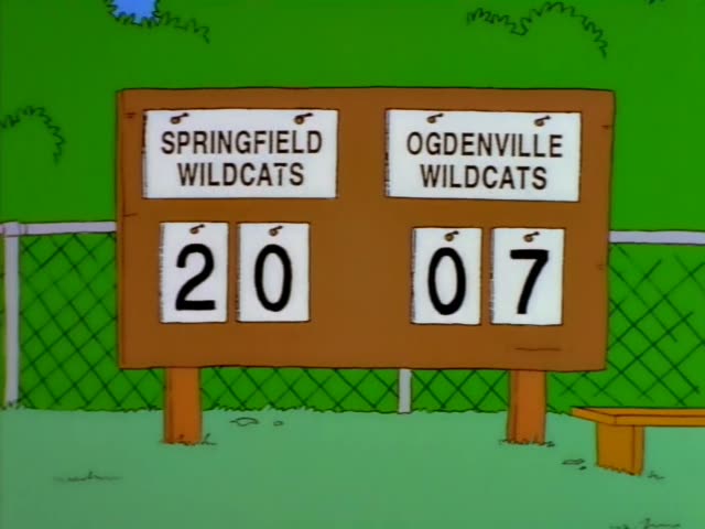 Ned Flanders sits on a bench at a football field beside young players in red helmets and jerseys, as a revolver points up…