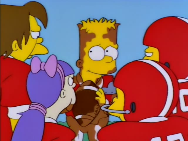 Bart grins and holds a football among a group of players in red jerseys on a sunny field with green turf, a blue sky…