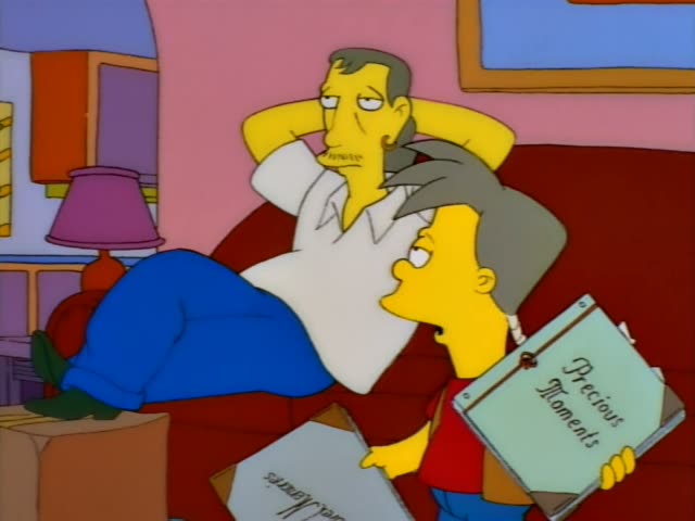 A dark-haired man with a moustache, in a white shirt and blue trousers, lies back on a red couch with his hands…