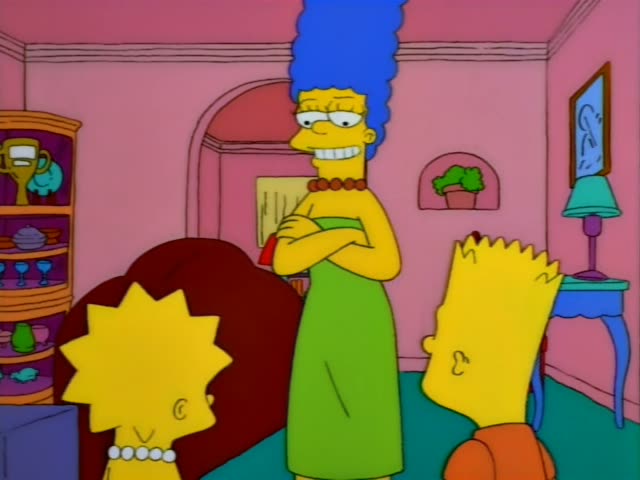 Marge stands with arms crossed beside Lisa and Bart, in an orange shirt, in a pink living room with a red armchair, a blue…
