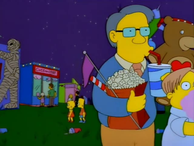 A bespectacled grey-haired man in a blue sweater holds popcorn and sips a drink while a child clutches pink cotton candy…
