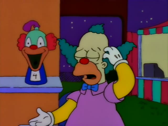 Krusty the Clown stands outdoors at night beside a booth with a giant clown head sign reading 4 on a pedestal to his left