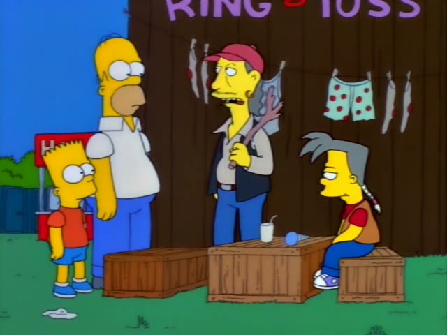 Homer and Bart stand in front of a wooden Ring Toss booth with clothes hanging on a line behind it, while a carnival vendor…