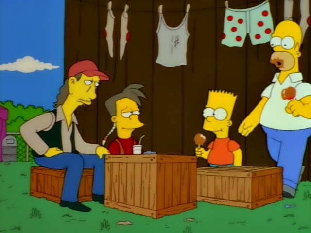 A long-haired man in a red cap and dark vest, and a thin boy with grey spiky hair and a red shirt, sit on wooden crates…
