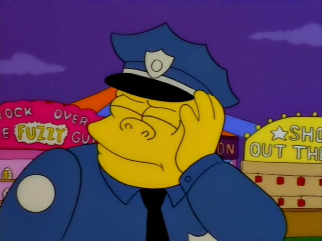 Chief Wiggum stands in front of a purple sky and a carnival backdrop with a pink "Fuzzy Gu" sign and a yellow…