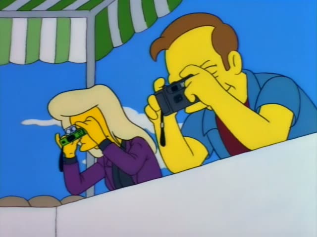 A blonde woman in a purple jacket and a man in a blue shirt peer through boxy devices beside a green-striped awning…
