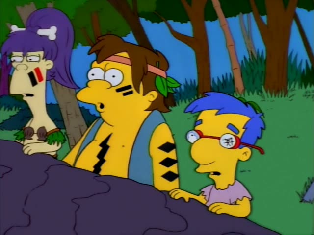 Milhouse sits beside a brown-haired man in a pink headband, leaf and blue vest with face paint and stripes…