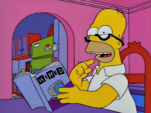 Homer sits at a pink-walled desk reading a WIRED magazine with a computer on its cover while Marge watches from a blue…