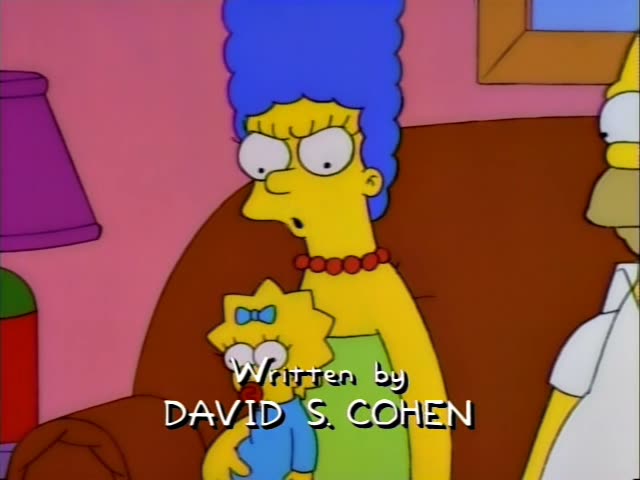 Marge stands beside Homer, who is seated on the brown couch, and both watch as Bart and Lisa lie on a colorful oval rug…