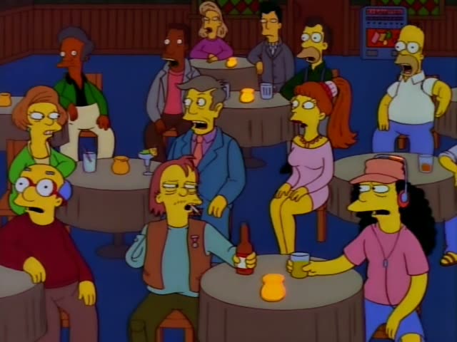 Inside Moe's bar, Carl sits at a round table beside Lenny's counterpart, a man with brown hair, suspenders and a green…