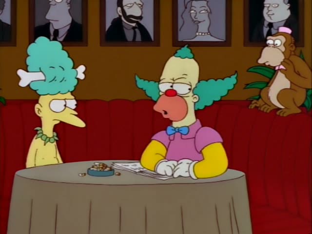 Krusty the Clown sits at a round table with a tablecloth in a restaurant booth, a red upholstered bench behind him…