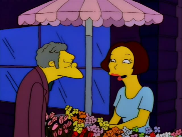 Moe stands at a flower stall under a pink scalloped umbrella, talking with a woman who has a short reddish-brown bob…