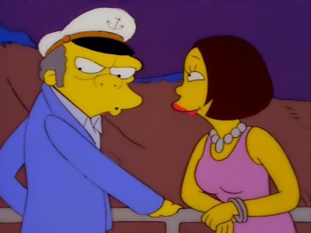 Mr. Burns stands at a railing beside a woman with a brown bob, pink dress and pearl necklace, gesturing and talking as she…