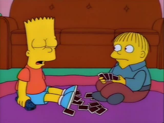 Bart and Ralph sit on a purple rug in front of a brown couch, with a scatter of face-down cards between them…