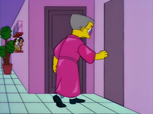 A grey-haired man with glasses in a pink robe walks down a pink hallway, reaches out to a doorknob, and pulls open a door…