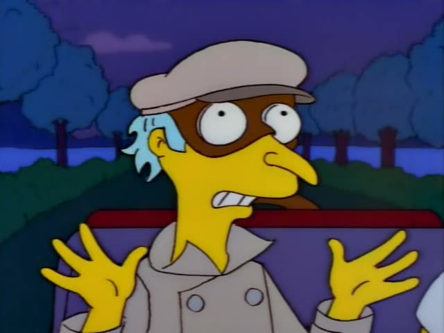 Mr. Burns goggles and a light trench coat with blue-grey hair at the sides, sits at the wheel of a car at dusk, gesturing…