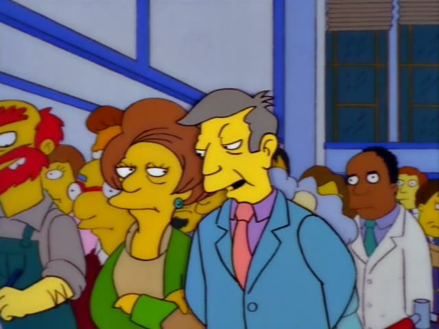 Principal Skinner stands in a crowd beside a woman with a brown bob, a green sweater and a green earring…