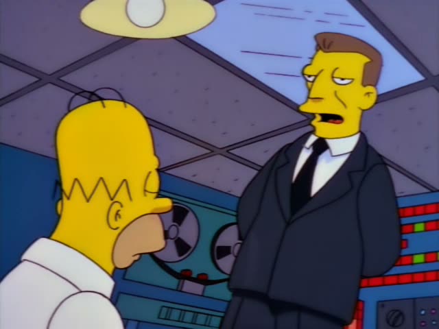 Homer sits in a chair in a control room of reel-to-reel tape machines and blinking panels, facing a sleek man in a dark suit…
